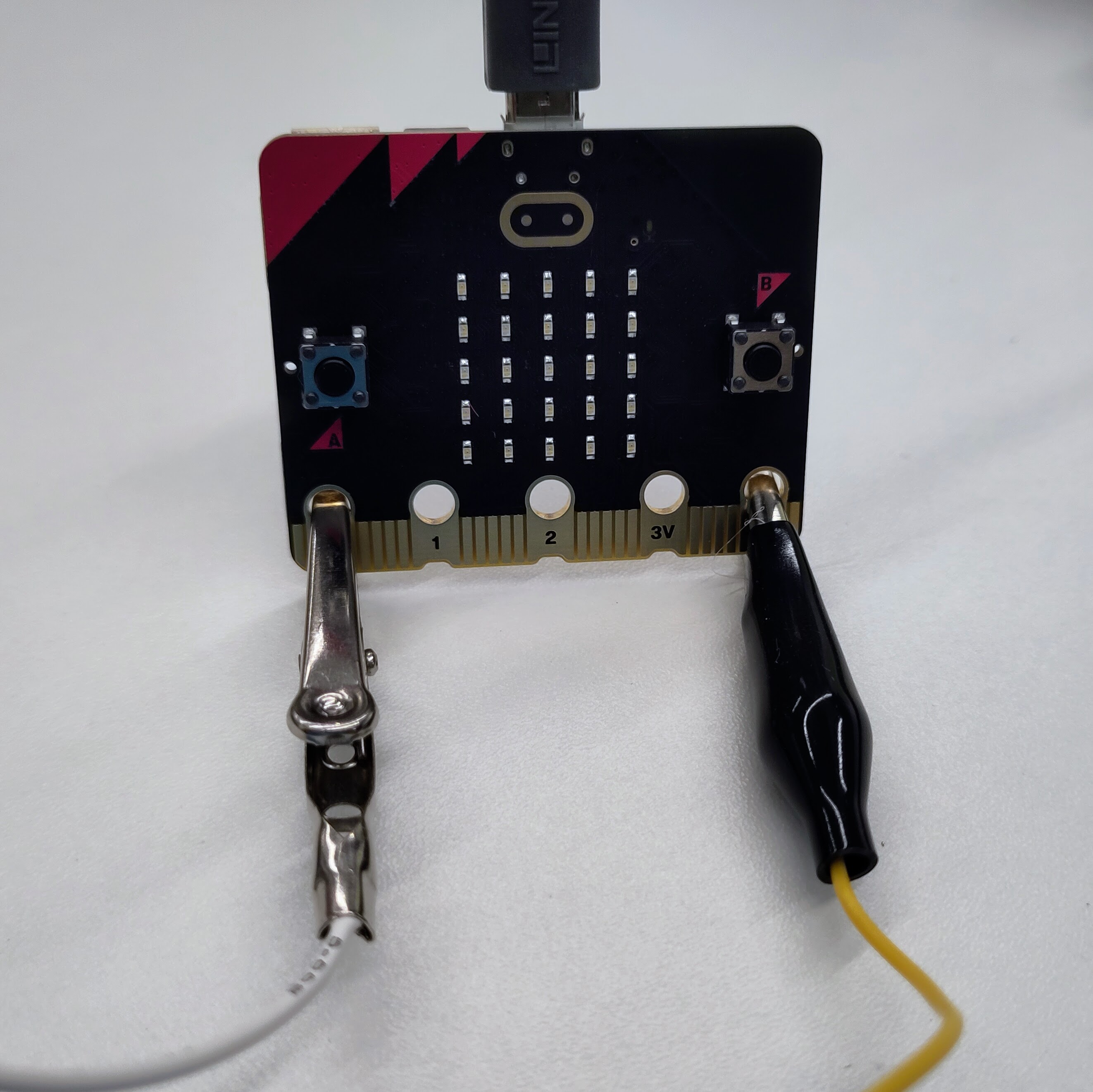 photograph showing a micro:bit with an uninsulated crocodile clip connected to pin 0 (the furthest left), and an insulated crocodile clip connected to GND (the furthest right)